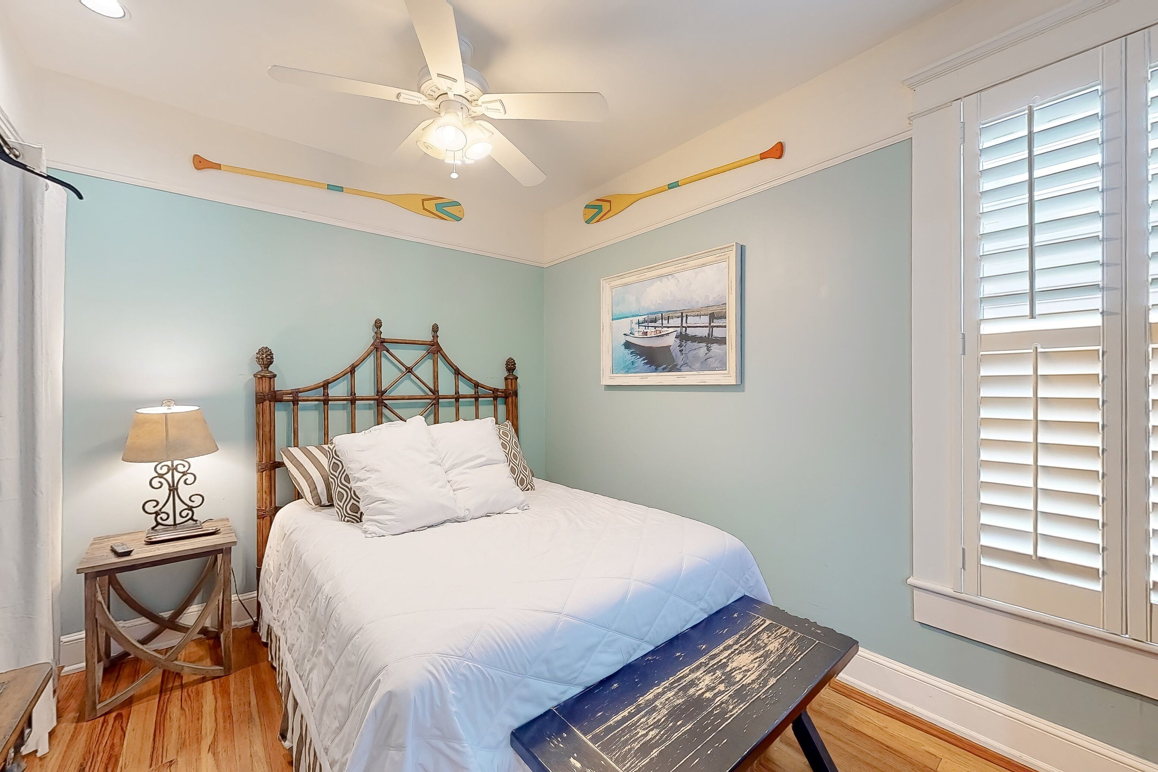 A bedroom with a bed, a nightstand, a lamp, a ceiling fan, and a window with blinds.