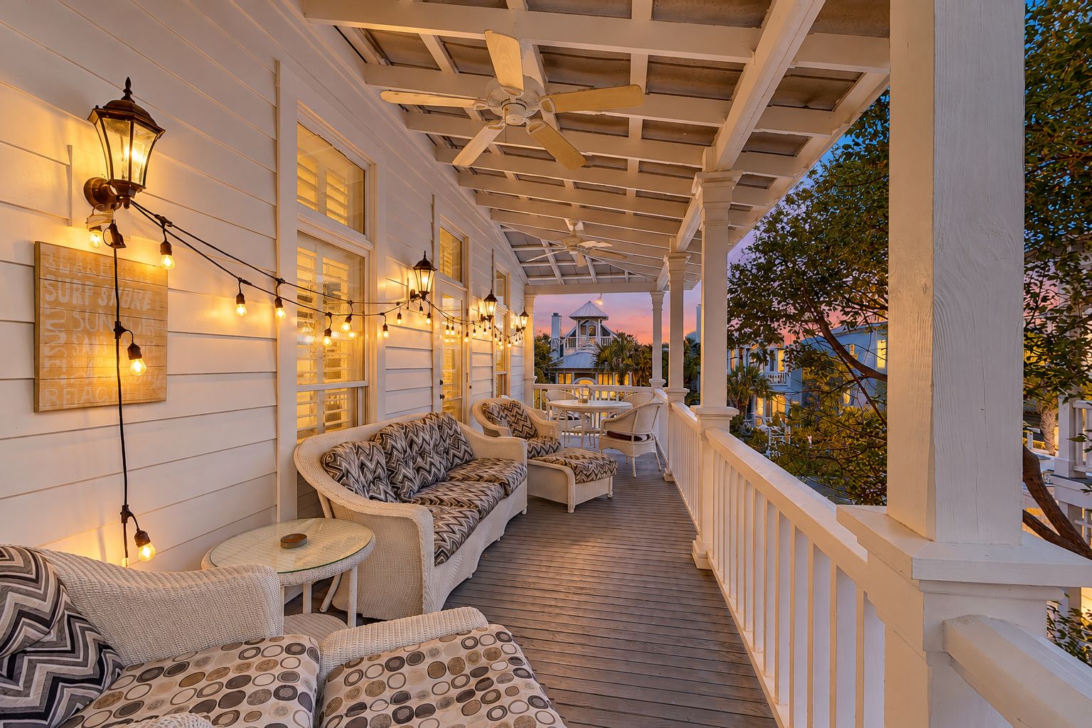 A covered porch with outdoor seating, string lights, and a view of a building in the background.