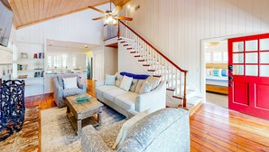 A spacious living area with a high ceiling, a staircase, and a red door. - Classic Coastal Home With Game Room & Private hot tub - Walk to Beaches (St. Simons Island)