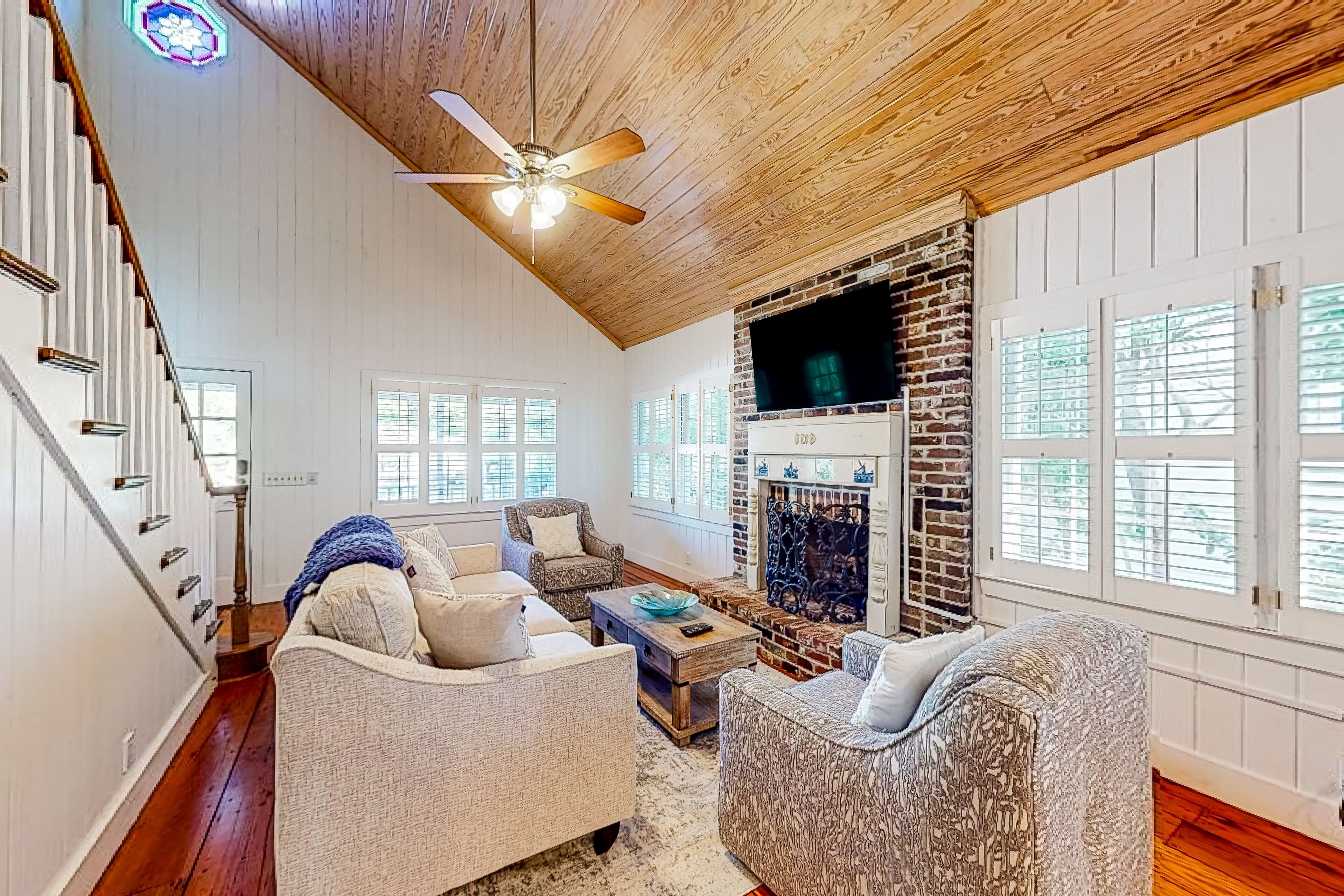 A spacious living room with a high ceiling, a fireplace, and a staircase.