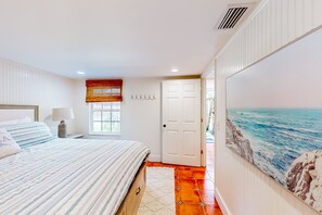 A bedroom with a bed, a window with blinds, a door, and a wall with a painting. - Classic Coastal Home With Game Room & Private hot tub - Walk to Beaches (St. Simons Island)
