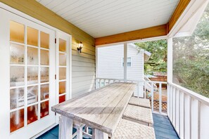A covered porch with a wooden table and benches, white siding, and a view of a house and greenery. - Classic Coastal Home With Game Room & Private hot tub - Walk to Beaches (St. Simons Island)