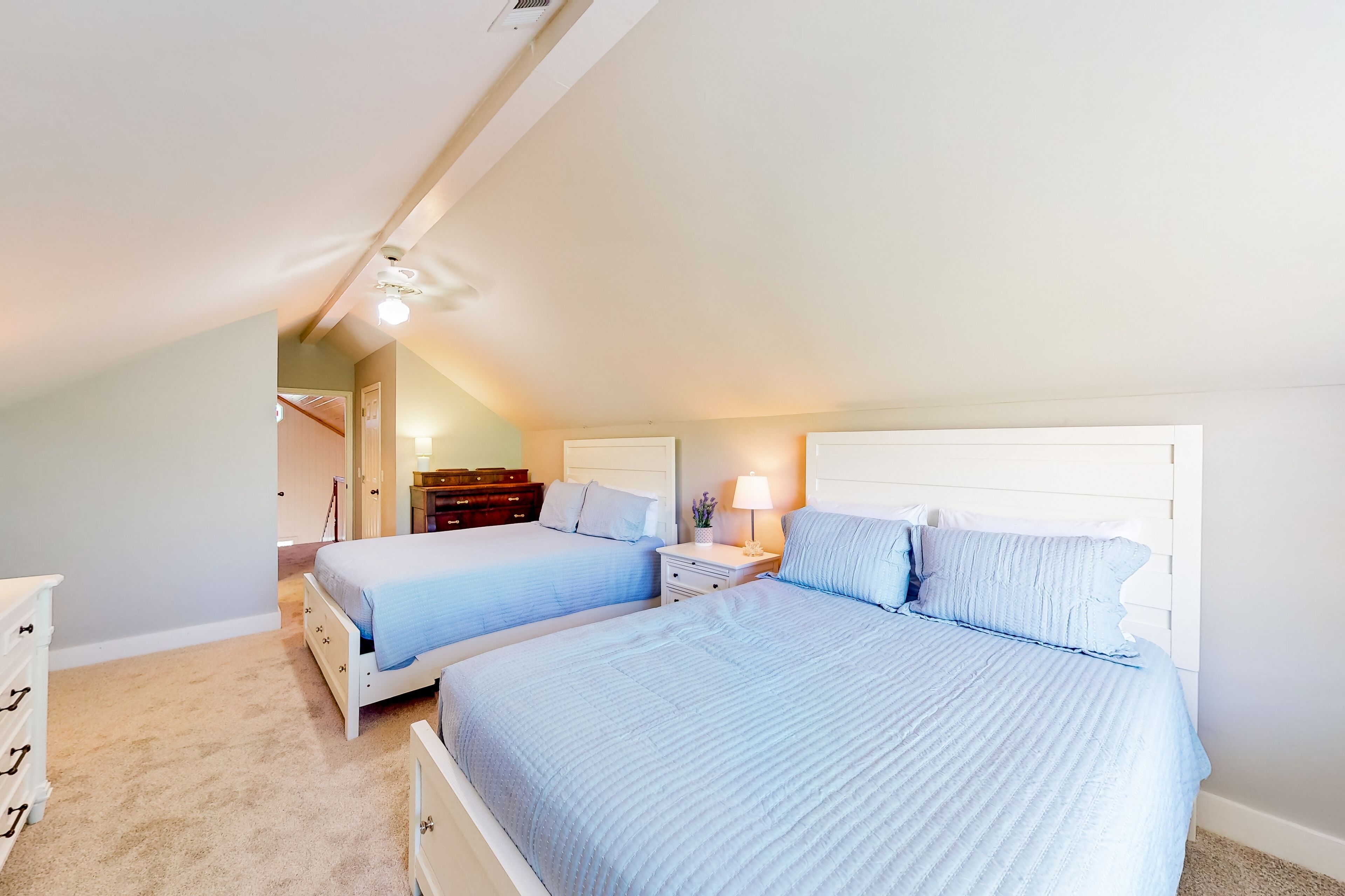 A bedroom with two beds, a dresser, and a nightstand with a lamp.