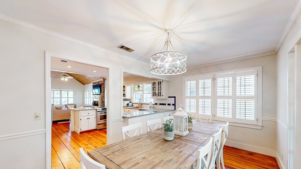 A spacious dining area with a wooden table and white chairs, a kitchen in the background, and a ceiling fan. - Classic Coastal Home With Game Room & Private hot tub - Walk to Beaches (St. Simons Island)