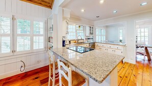 A spacious kitchen with a granite countertop, wooden flooring, and white cabinetry. - Classic Coastal Home With Game Room & Private hot tub - Walk to Beaches (St. Simons Island)