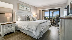 A bedroom with a large bed, a nightstand, a dresser, and a balcony with a view of the ocean. - Completely Renovated Oceanfront Condo W/washer/dryer & Shared Pool/tennis (Fernandina Beach)