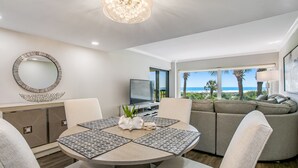 A modern living room with a round table, beige sofas, and a large window offering a view of the ocean. - Completely Renovated Oceanfront Condo W/washer/dryer & Shared Pool/tennis (Fernandina Beach)