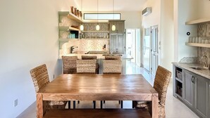 Un'ampia sala da pranzo con un lungo tavolo in legno e sedie in vimini, una cucina con elettrodomestici moderni e una grande finestra, e un'atmosfera luminosa e ariosa.