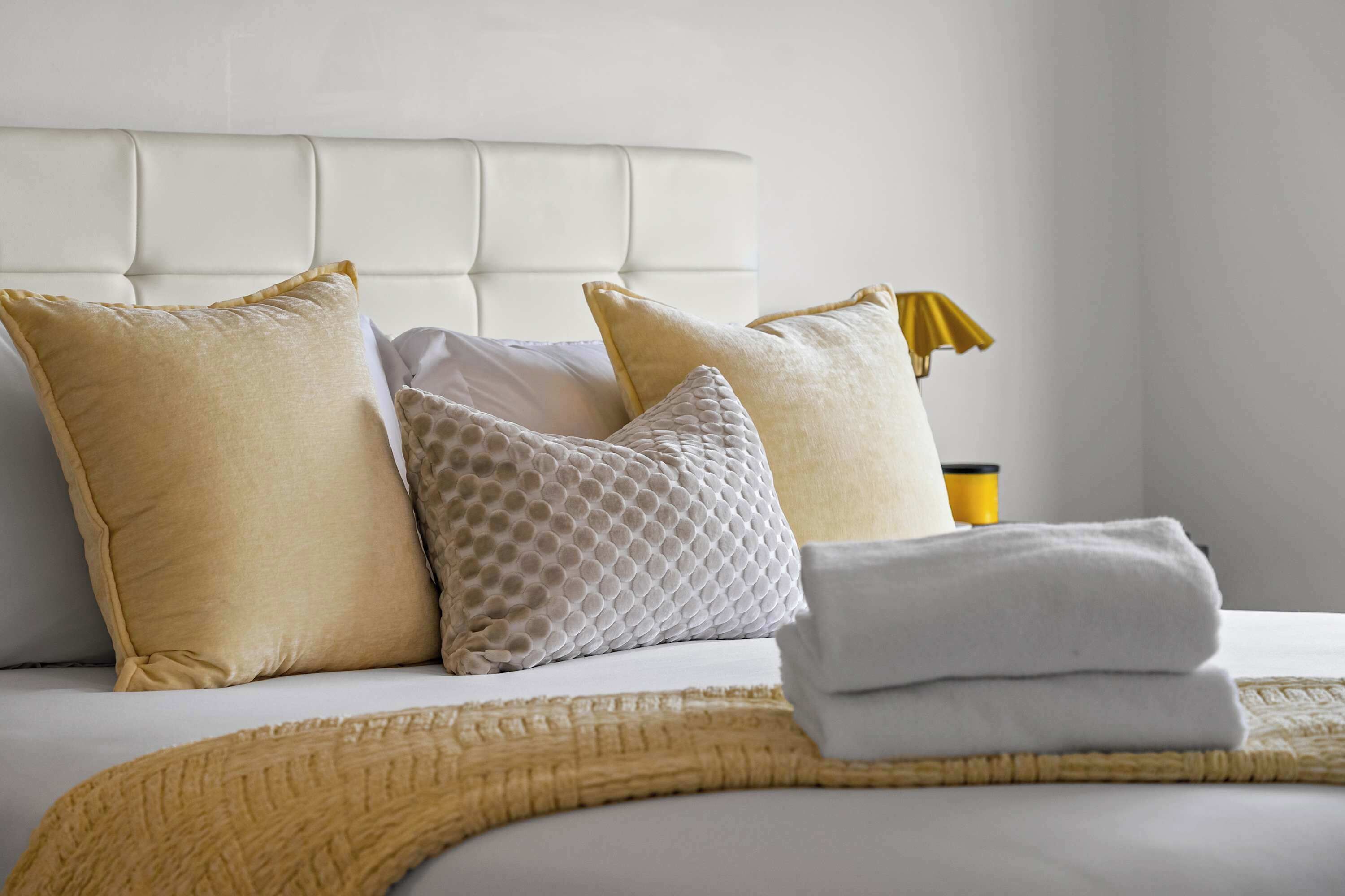 A neatly made bed with a white headboard, multiple pillows, and a folded white towel.