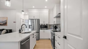A modern kitchen with white cabinetry, stainless steel appliances, and a central island. - 5BR Family Home w Kids Play Den (Calgary)