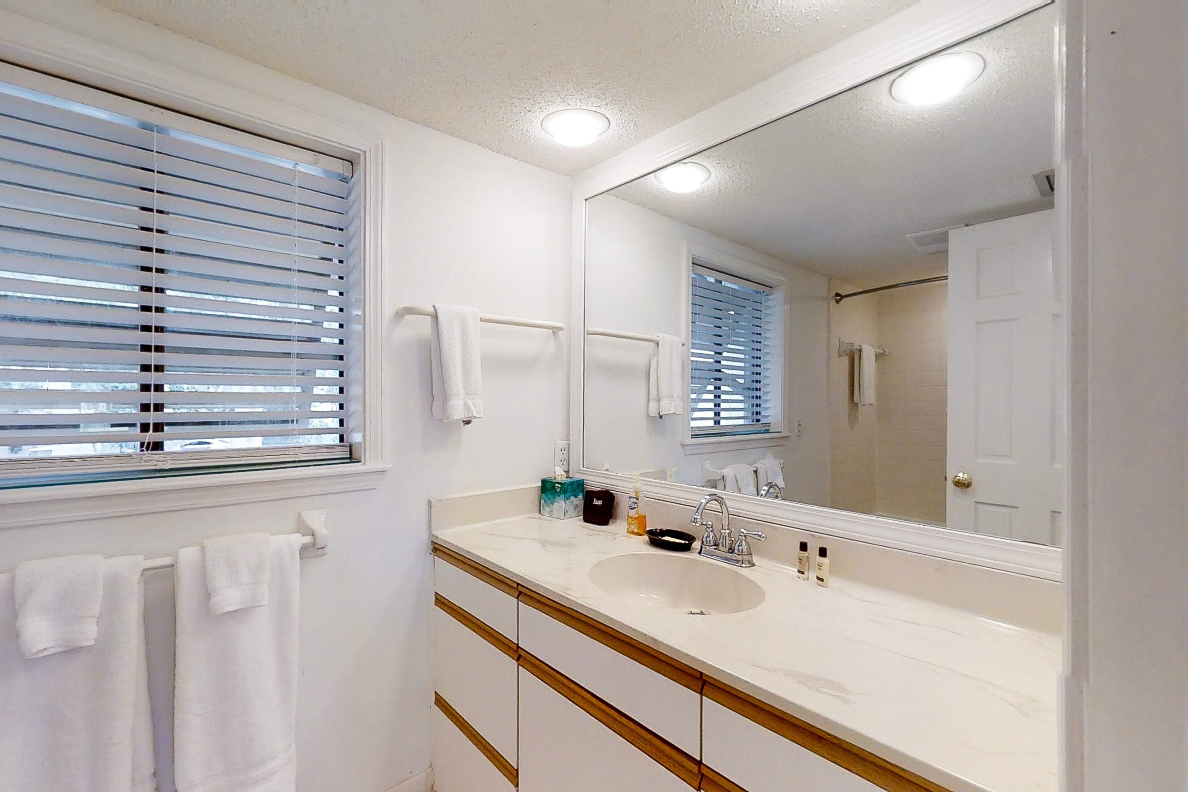 A bathroom with a white sink, a mirror, and a window with blinds.