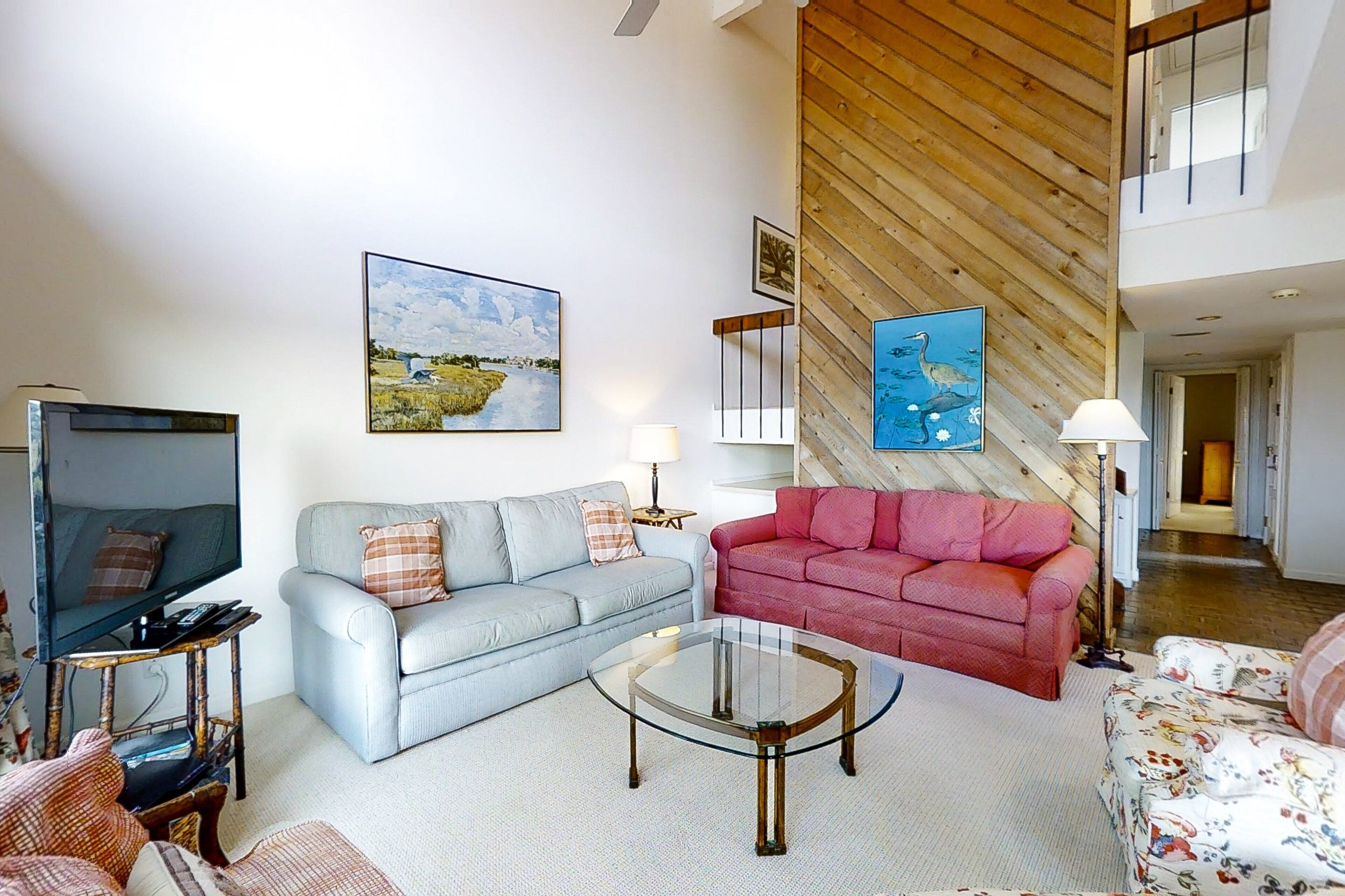A living room with a television, two sofas, a glass coffee table, and artwork on the walls.