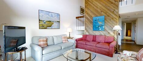 A living room with a television, two sofas, a glass coffee table, and artwork on the walls.