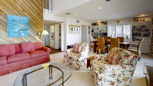 A spacious living room with a red sofa, floral armchairs, a glass coffee table, and a dining area with a wooden table and chairs. - Amelia Island Plantation Townhome With Amazing Marsh Views, Wifi & Shared Pool (Fernandina Beach)