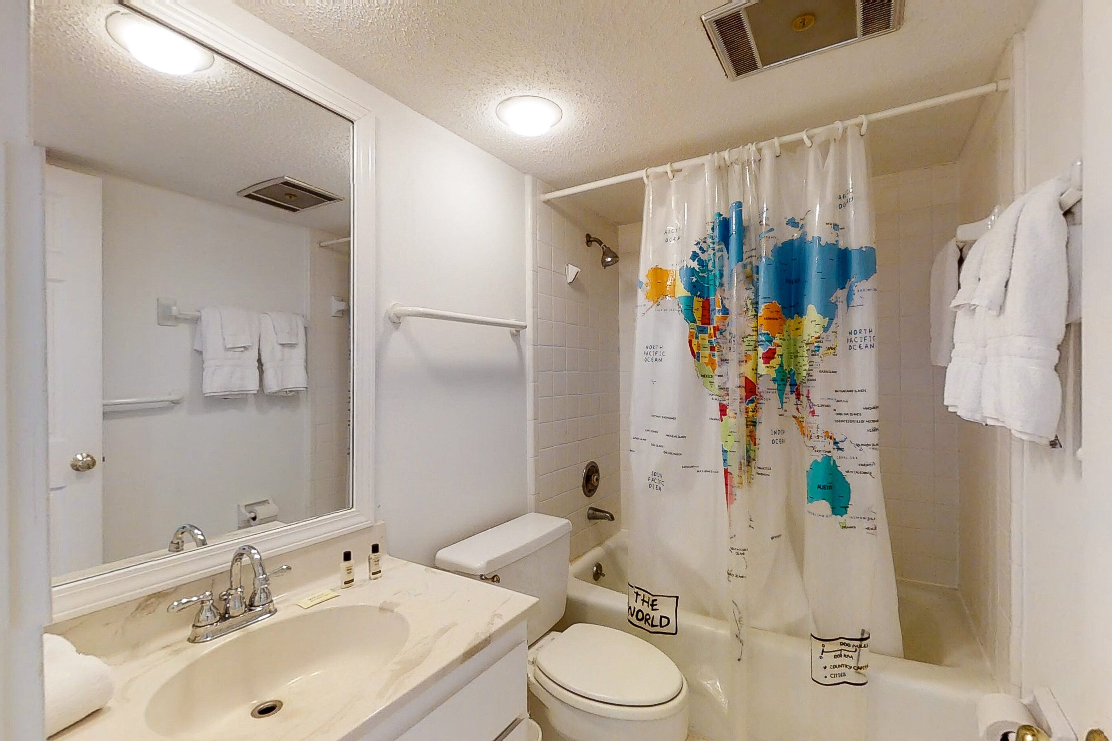 A bathroom with a sink, mirror, toilet, and shower curtain with a world map design.