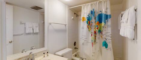 A bathroom with a sink, mirror, toilet, and shower curtain with a world map design.