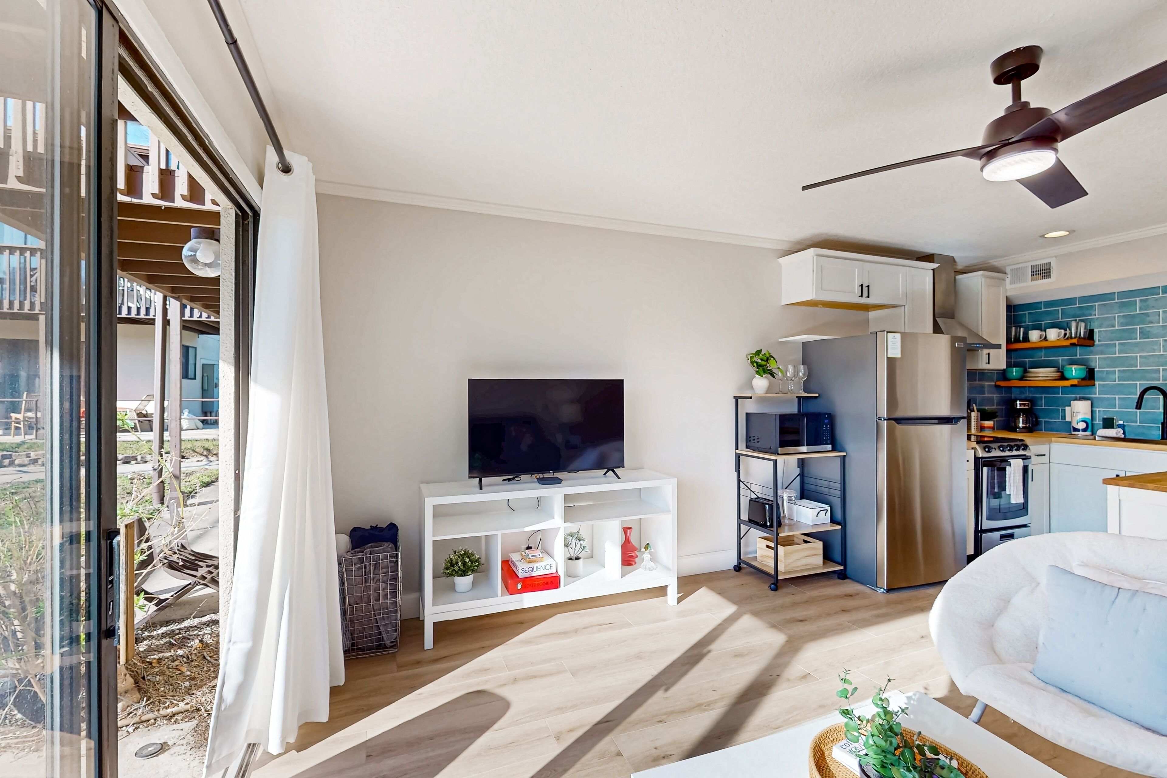 Una sala de estar moderna con televisor de pantalla plana, mueble blanco para entretenimiento y ventilador de techo.