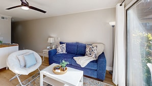 Ein modernes Wohnzimmer mit einem blauen Sofa, einem weißen Sessel, einem Deckenventilator und einem großen Fenster.