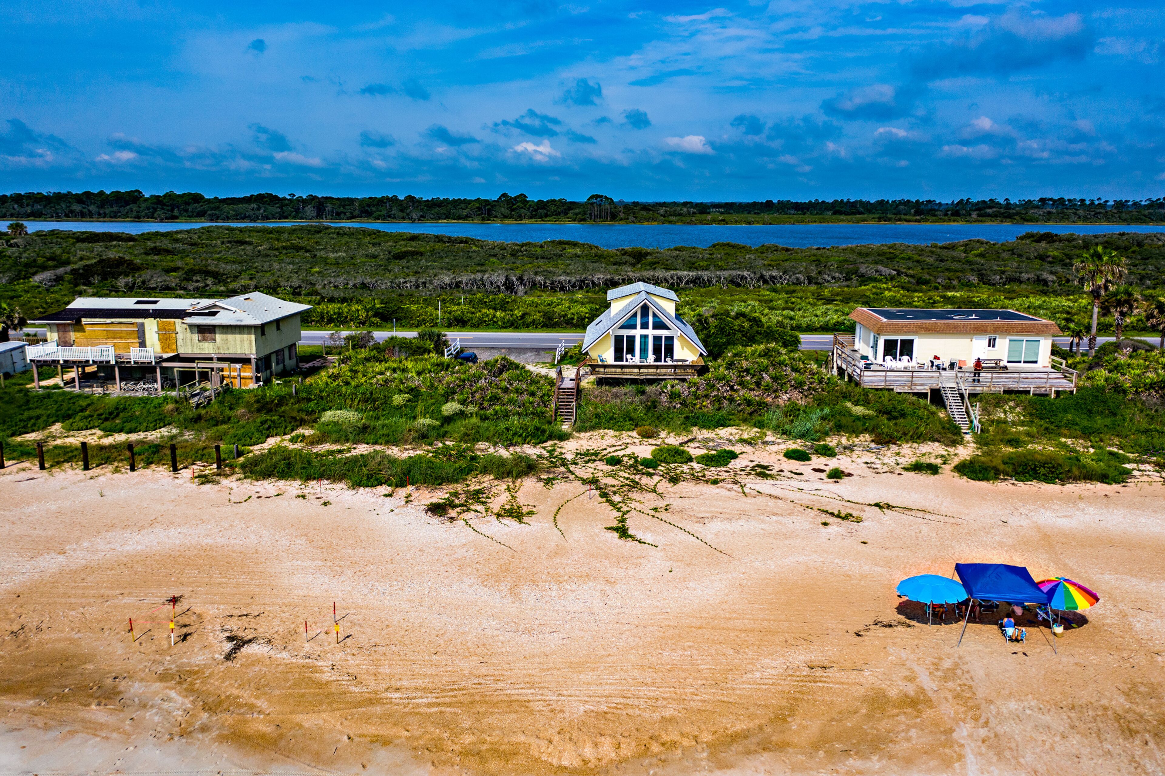 A beachfront property with a large house, a smaller house, and a beach umbrella.