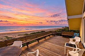Une terrasse en bois avec des sièges extérieurs et une vue sur la plage au coucher du soleil.