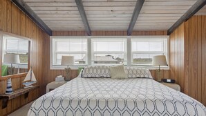 A bedroom with a large bed, wooden walls, and three windows. - A-frame Beach House Steps From the Ocean With Deck & Central AC (Ponte Vedra Beach)