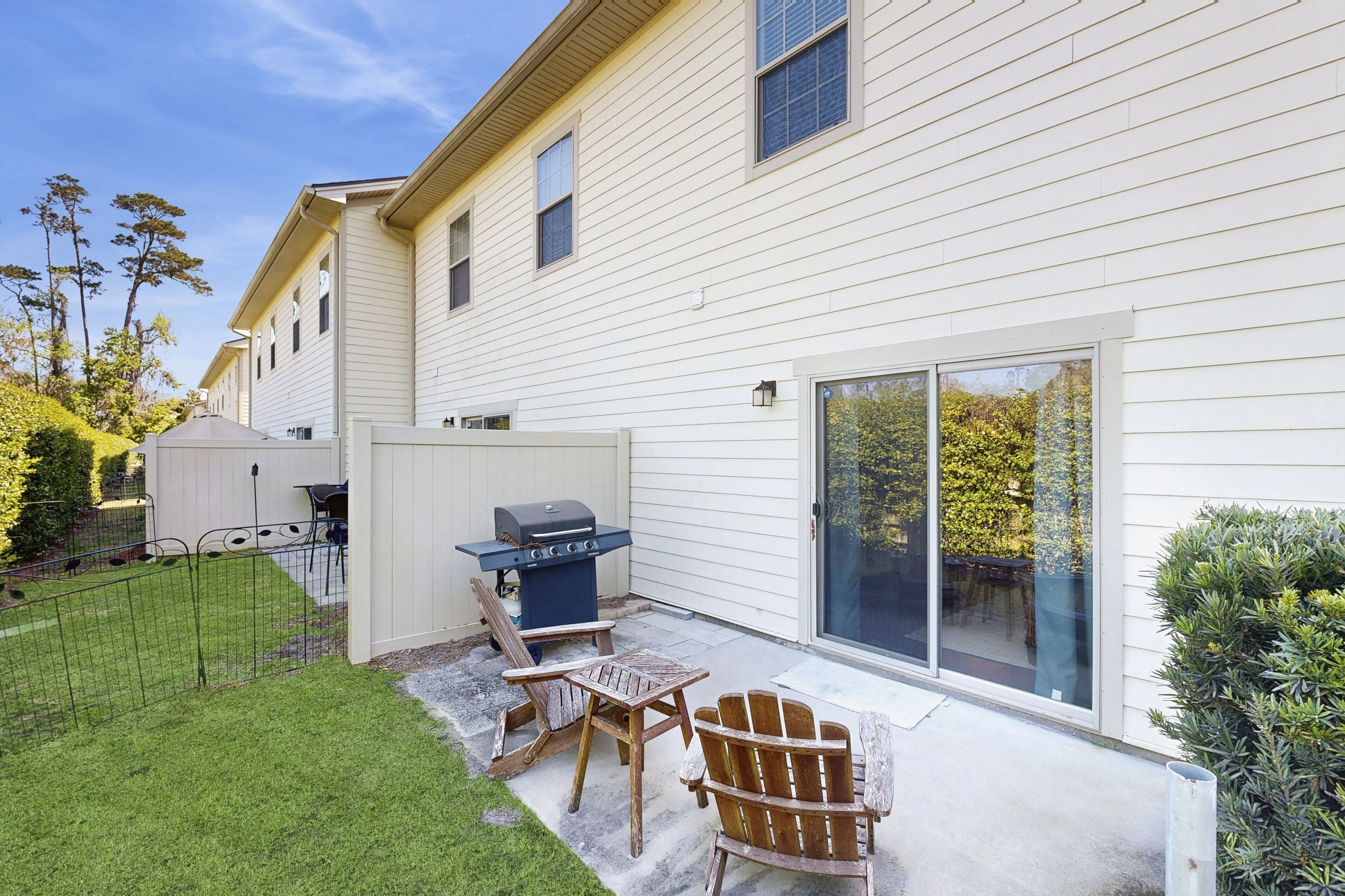 A patio with a grill, two Adirondack chairs, and a small table.