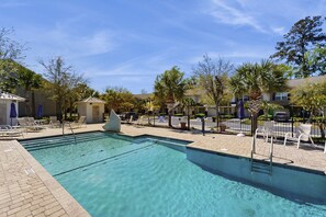 Una piscina rectangular con agua cristalina, rodeada de sillas de descanso y un pequeño pabellón.