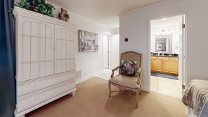 Une pièce avec une armoire blanche, une chaise dotée d’un coussin à motifs et une vue sur un coin cuisine.