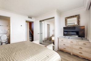 Une chambre à coucher avec un lit, une commode, une télévision et un miroir.