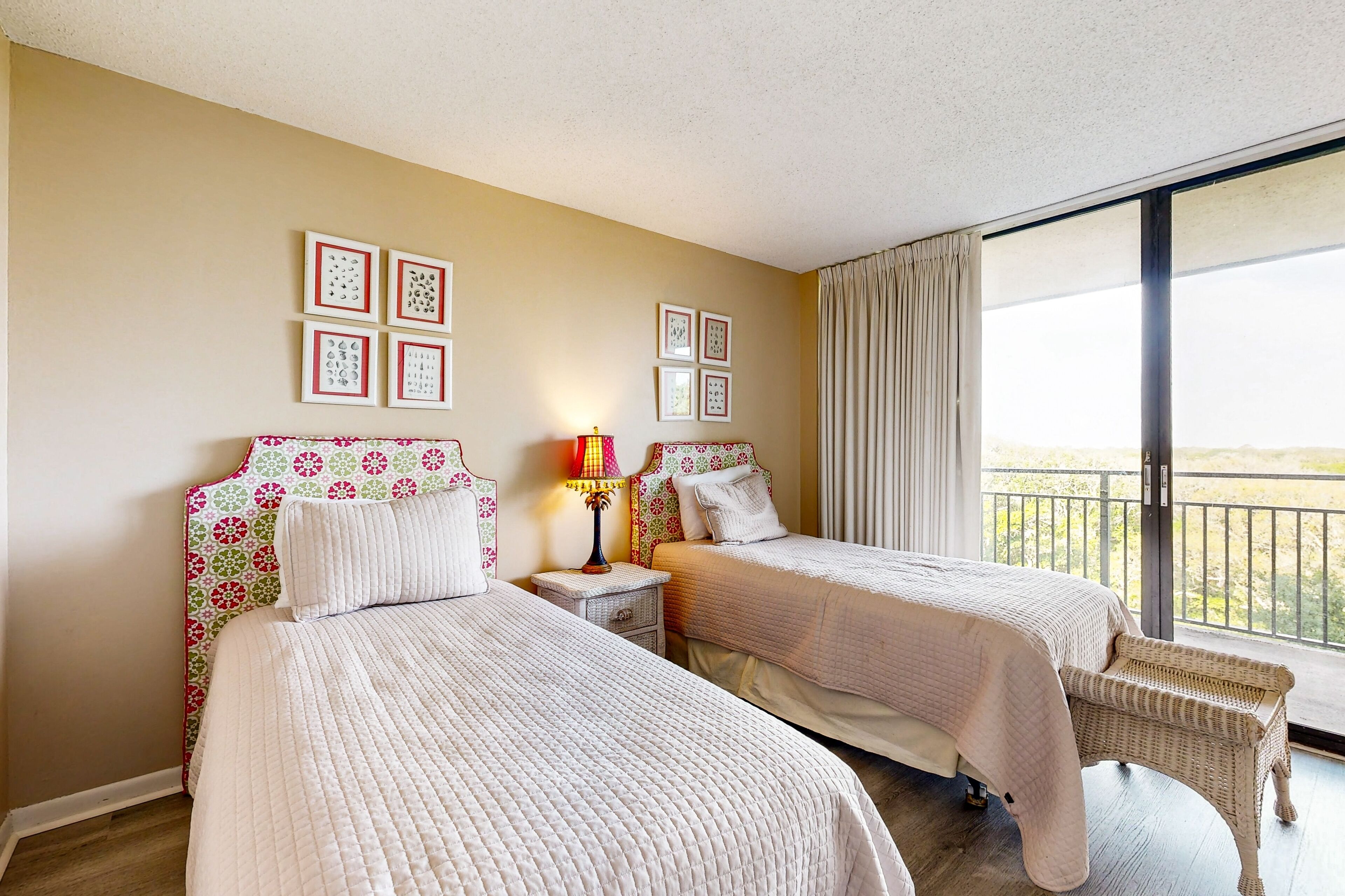 A hotel room with two beds, a nightstand with a lamp, and a view of the outdoors through a large window.