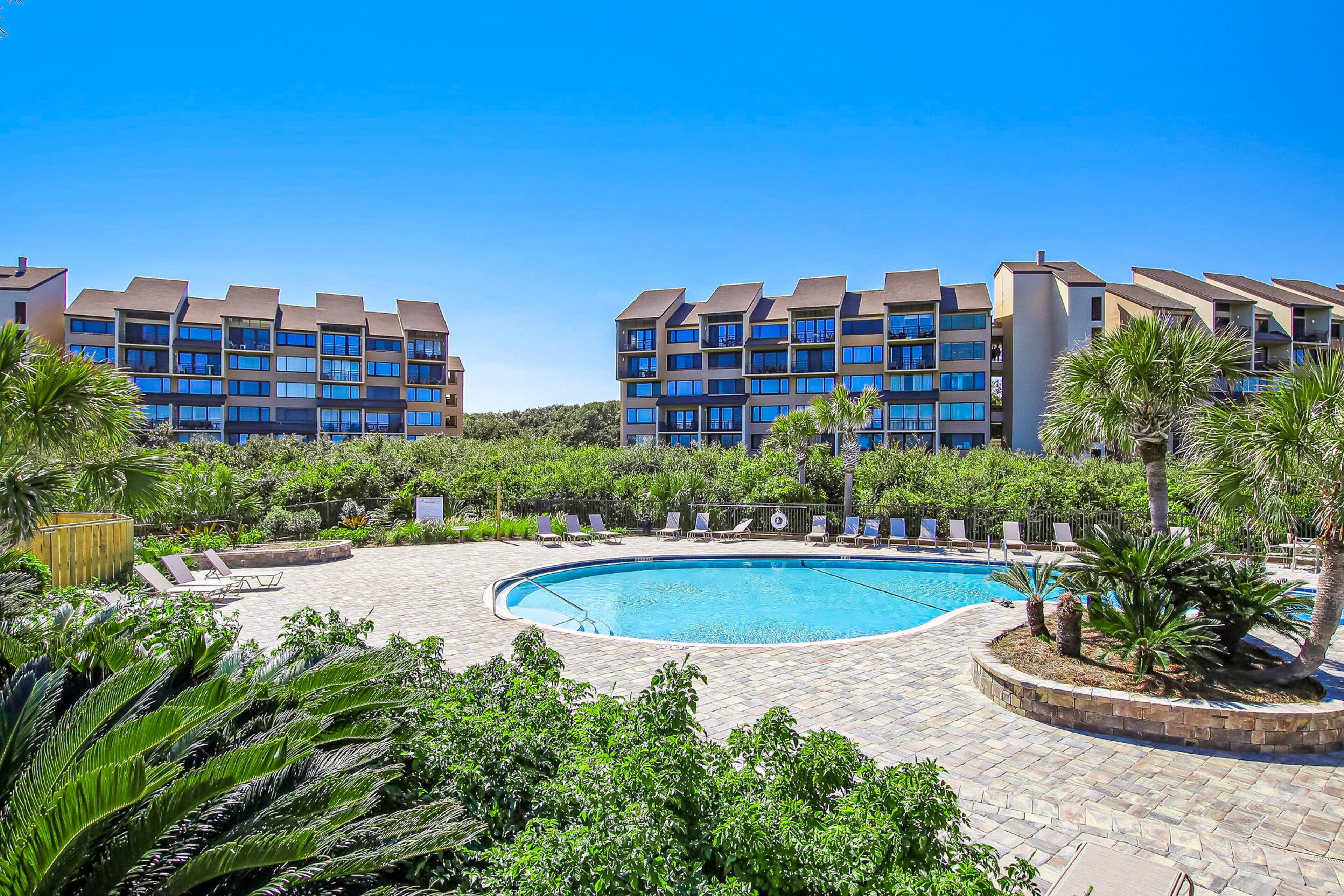 A resort with a swimming pool surrounded by palm trees and lounge chairs.