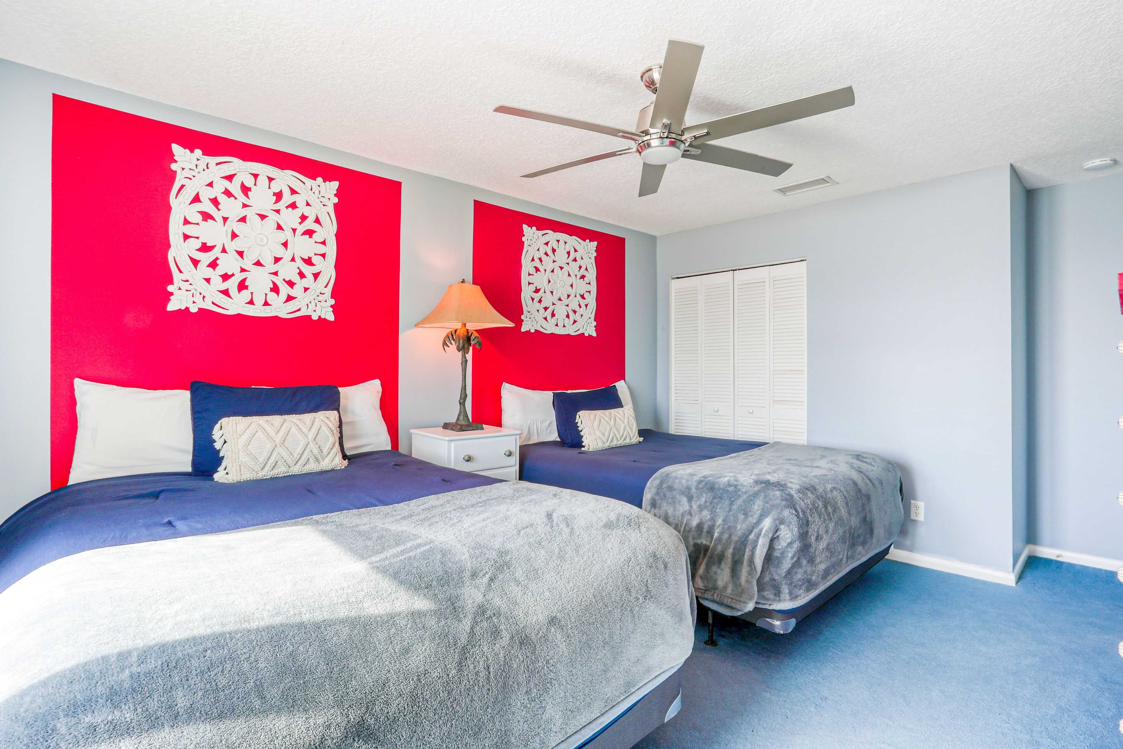 A bedroom with two beds, a ceiling fan, and a nightstand with a lamp.