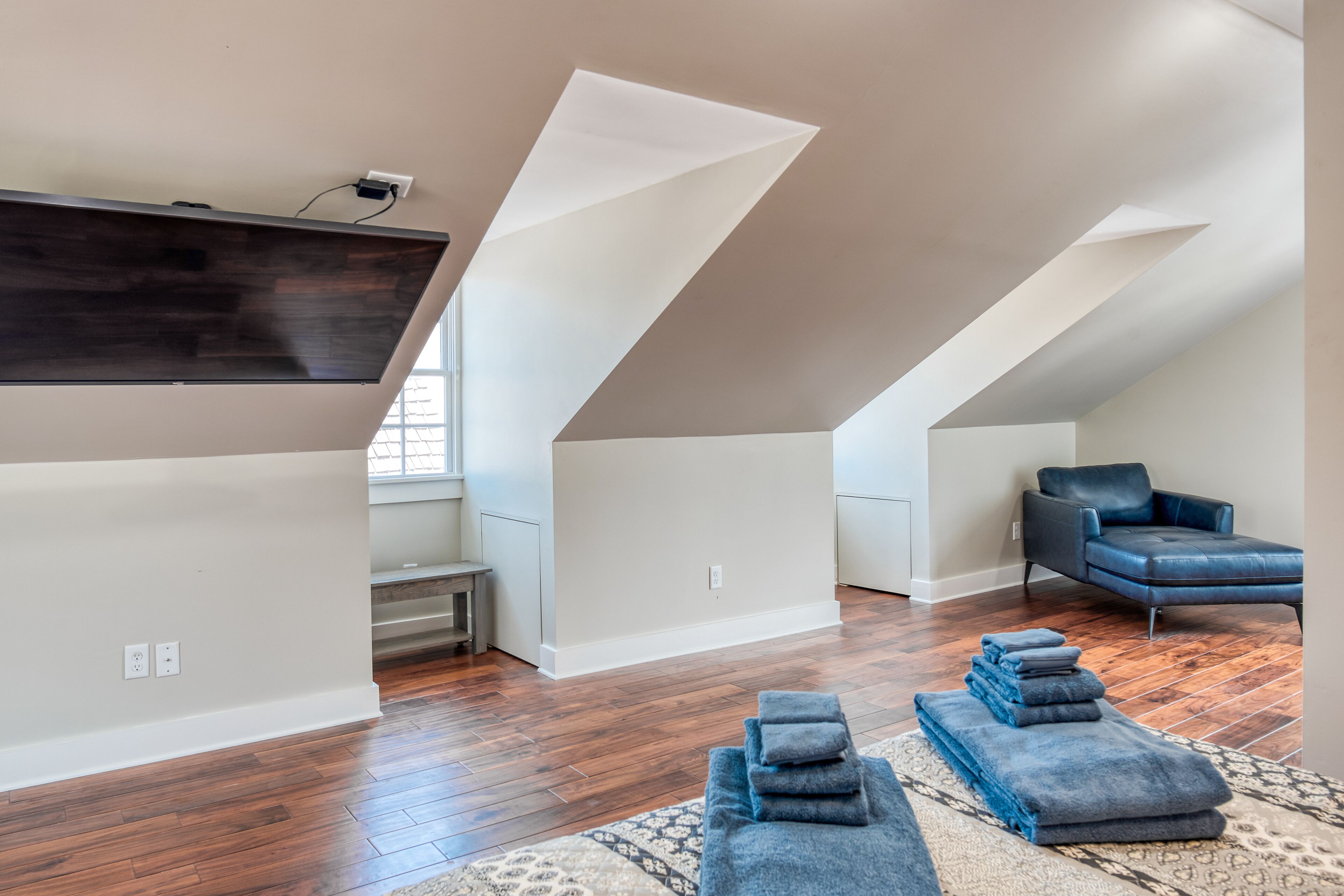 A spacious loft with high ceilings, a large window, a dark wooden wall, a blue leather chair, and a patterned rug.