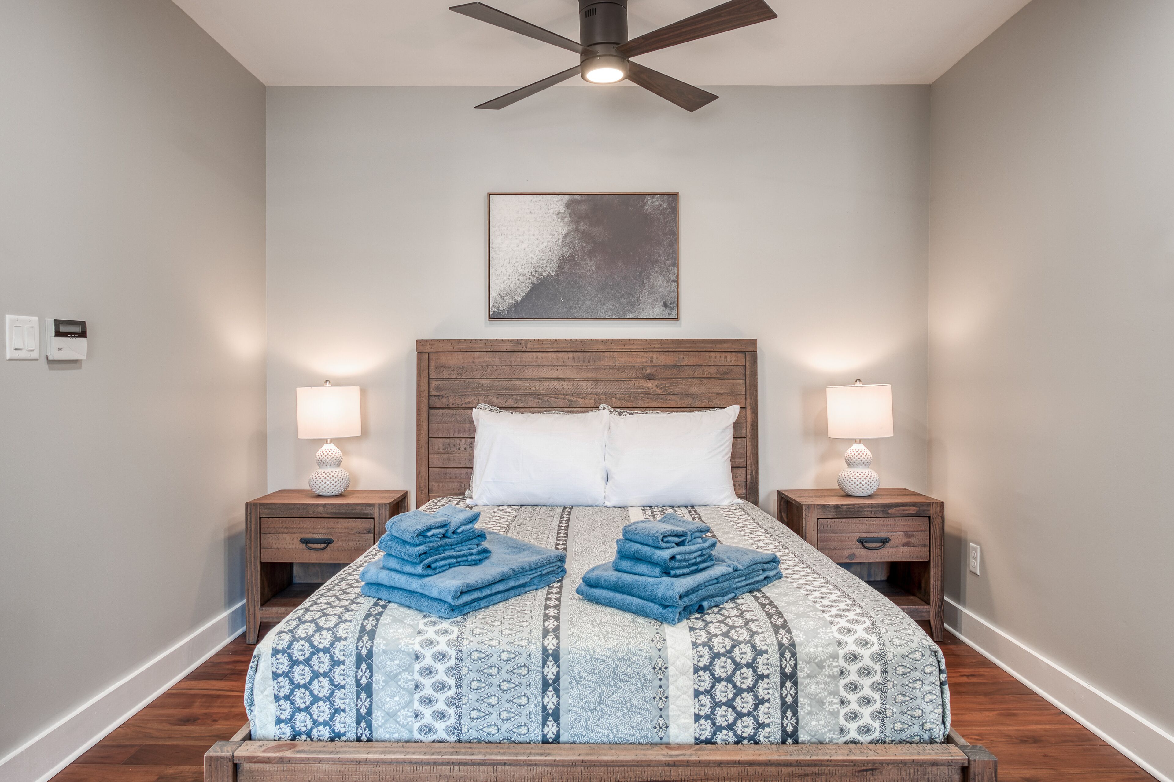 A neatly made bed with blue towels, a wooden headboard, and two bedside lamps.