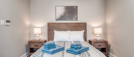 A neatly made bed with blue towels, a wooden headboard, and two bedside lamps.