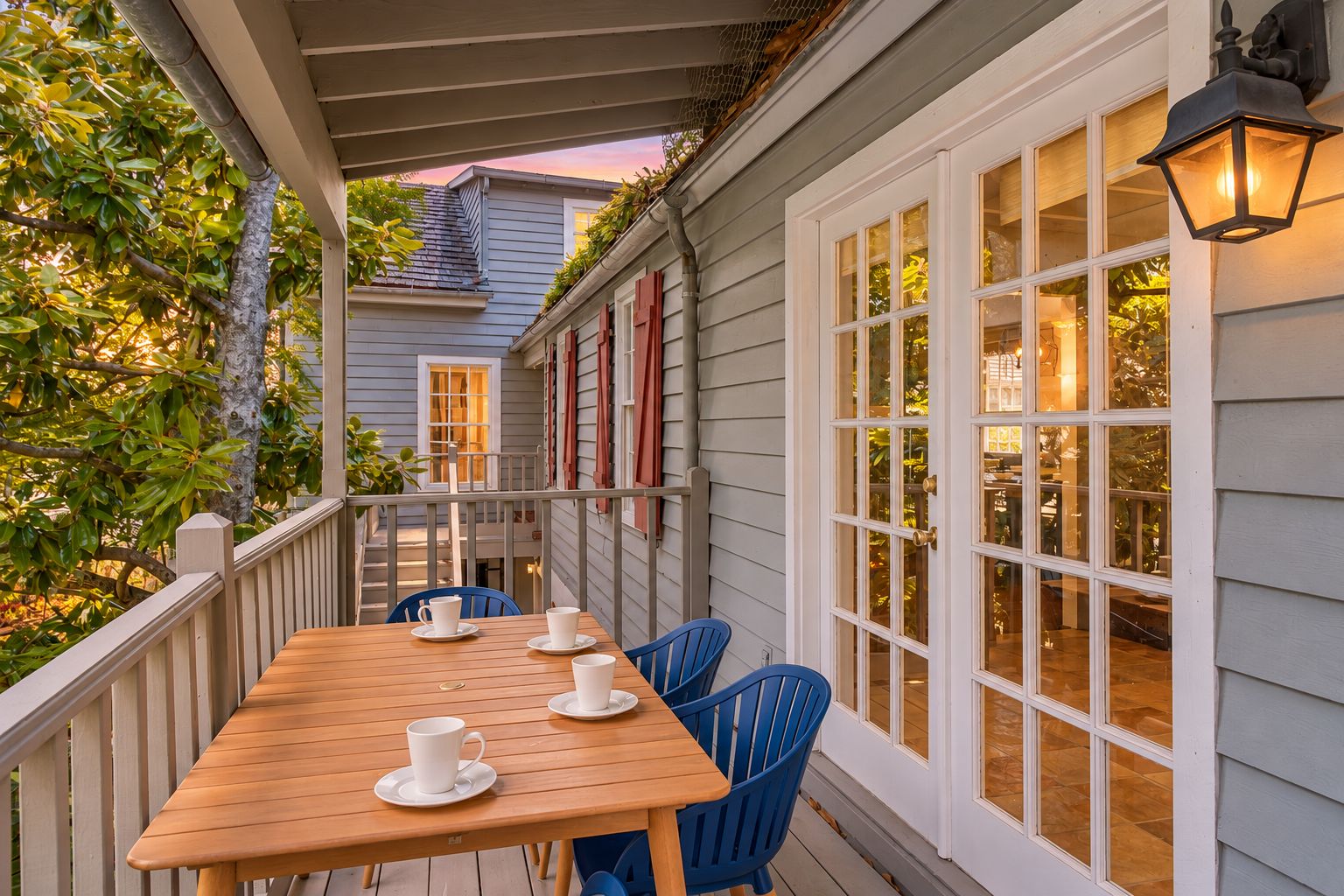 A wooden deck with a table and chairs, a covered area with a railing, and a building with large windows and a door.