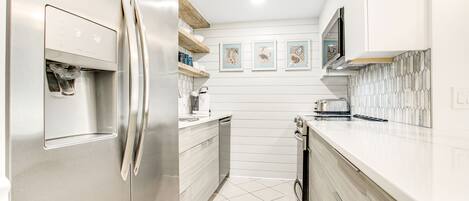 Una cocina moderna con electrodomésticos de acero inoxidable, armarios blancos y salpicadero de azulejos.