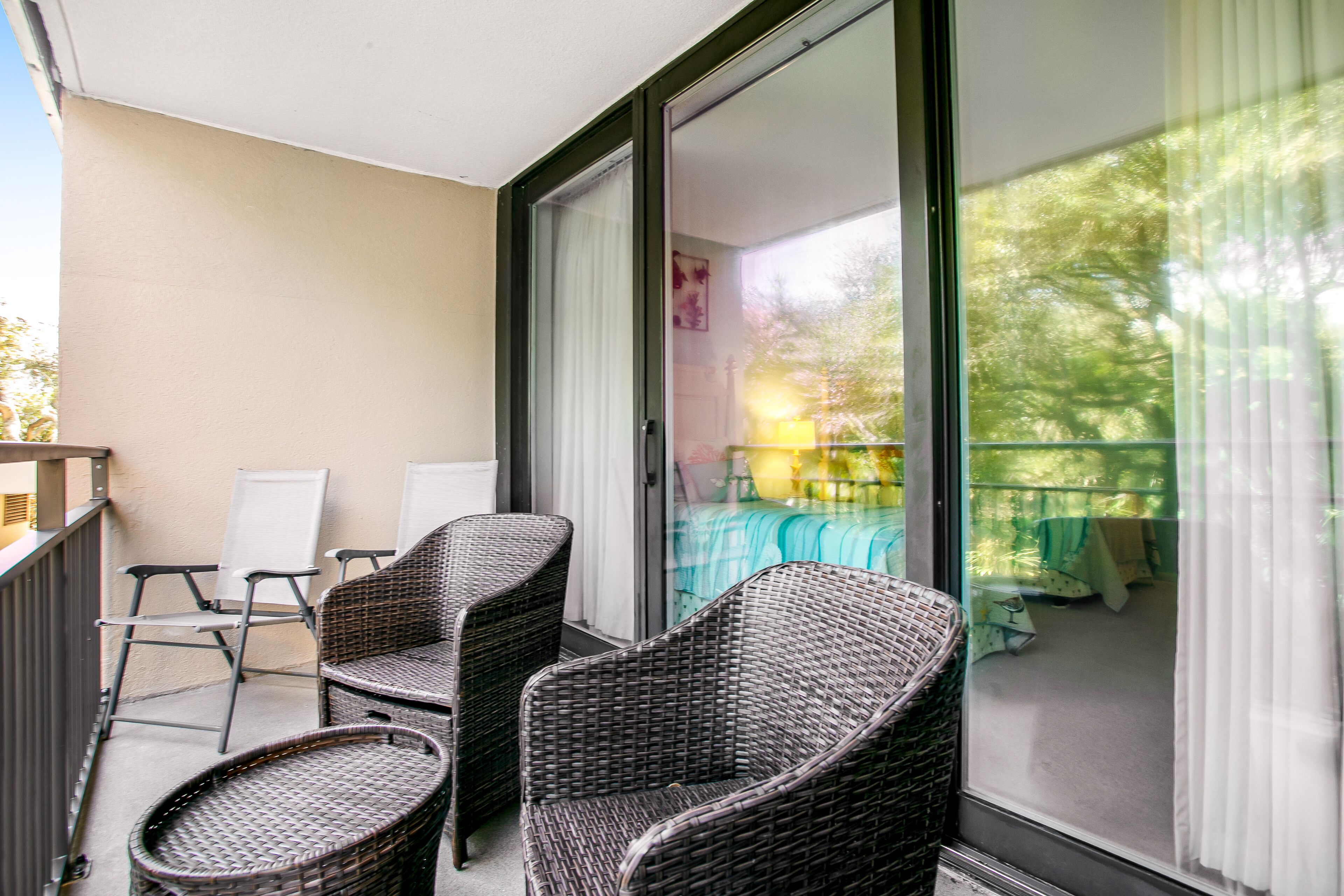 A balcony with wicker furniture, a sliding glass door, and a view of a green outdoor area.