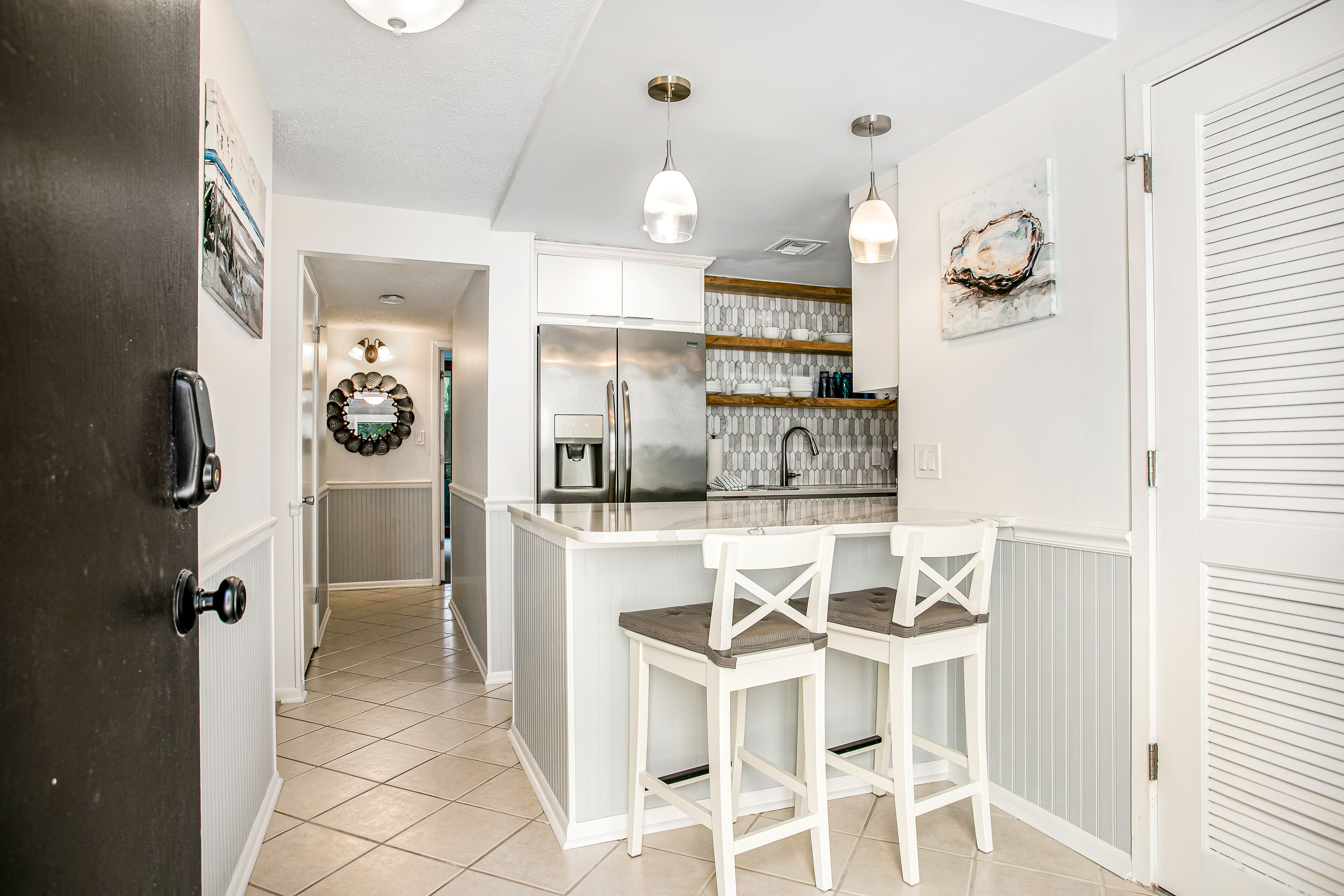 A kitchen with a central island, white bar stools, pendant lighting, and a refrigerator.