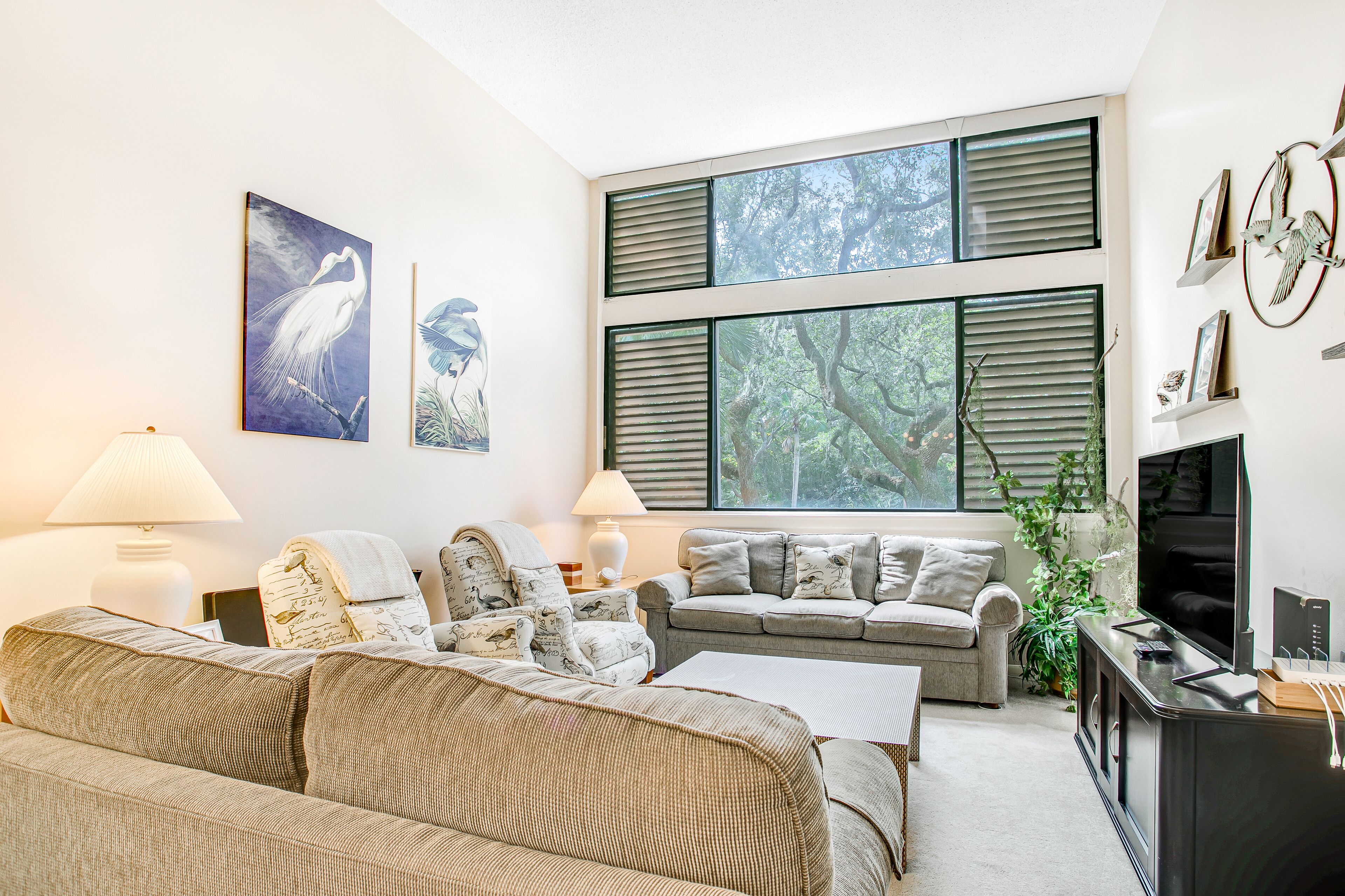 A modern living room with a large window, a flat-screen TV, and a sofa set.