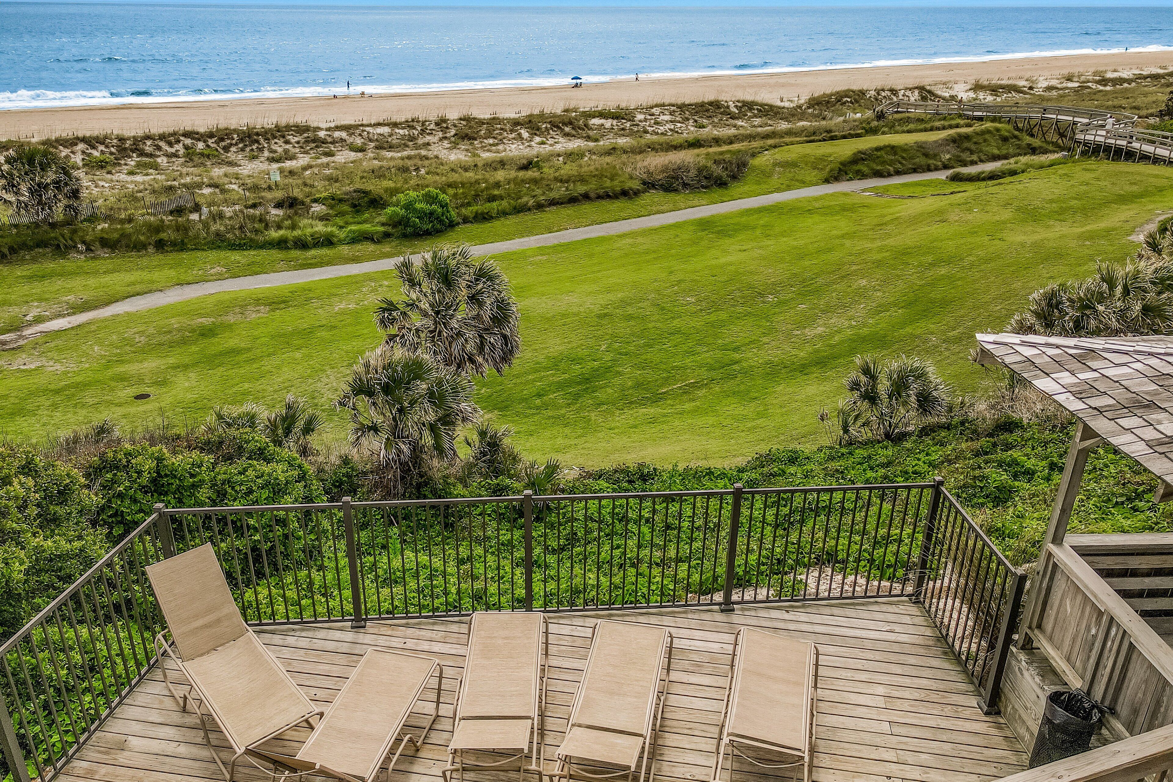 Une terrasse avec des chaises longues donnant sur un terrain de golf et une plage.