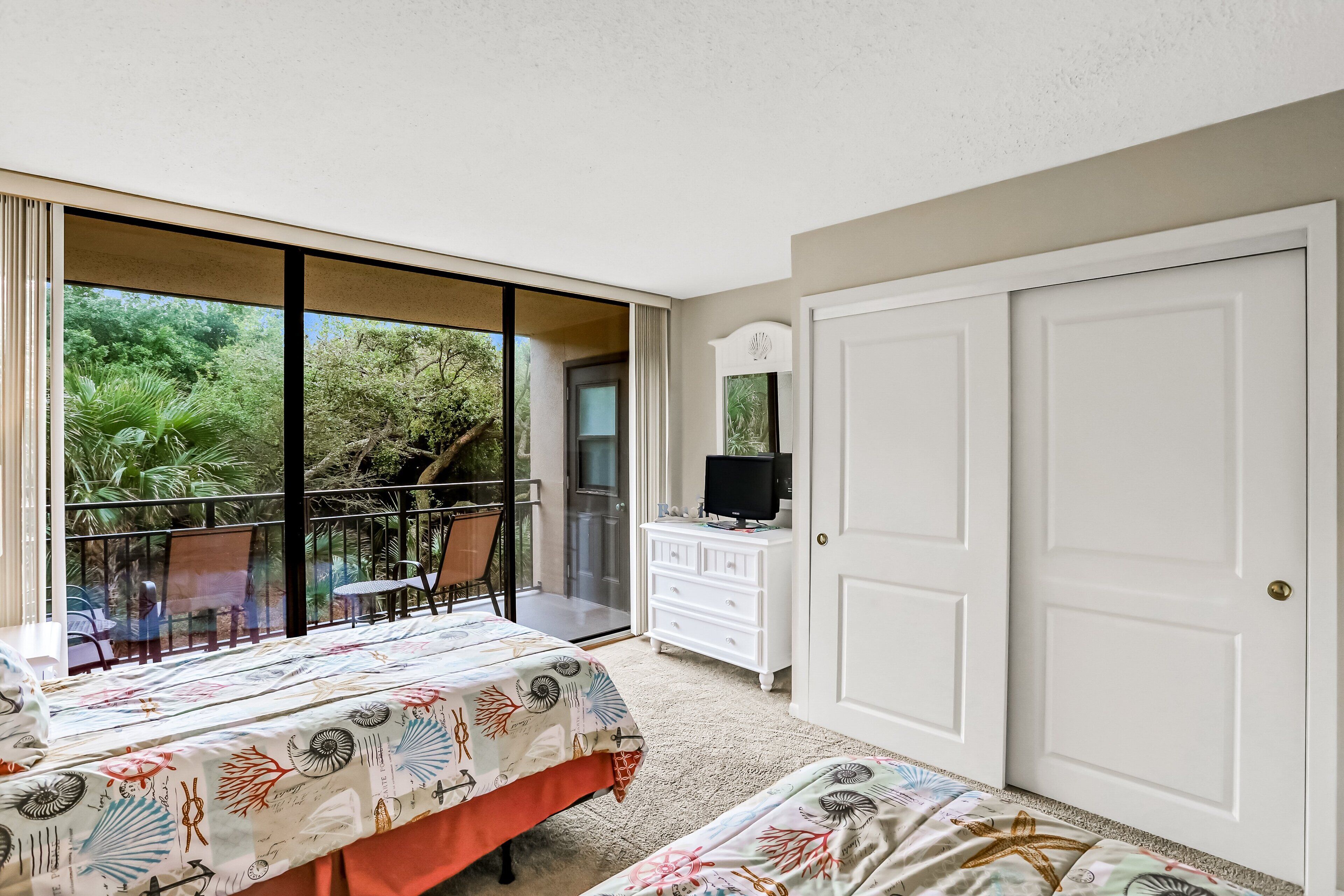 Een slaapkamer met twee bedden, een televisie op een dressoir en een balkon met uitzicht op groen.