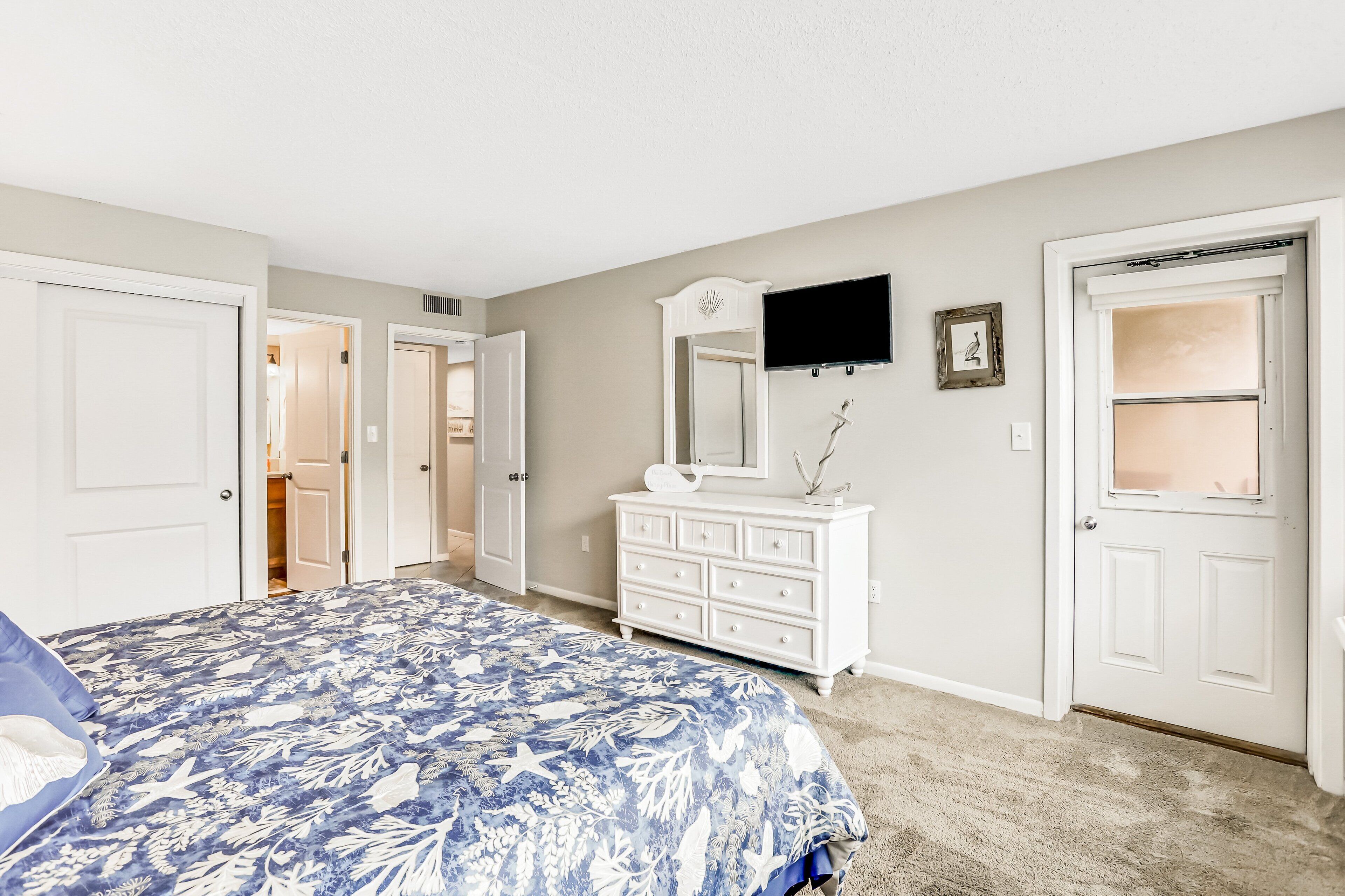 A bedroom with a bed, dresser, TV, and a door leading to another room.