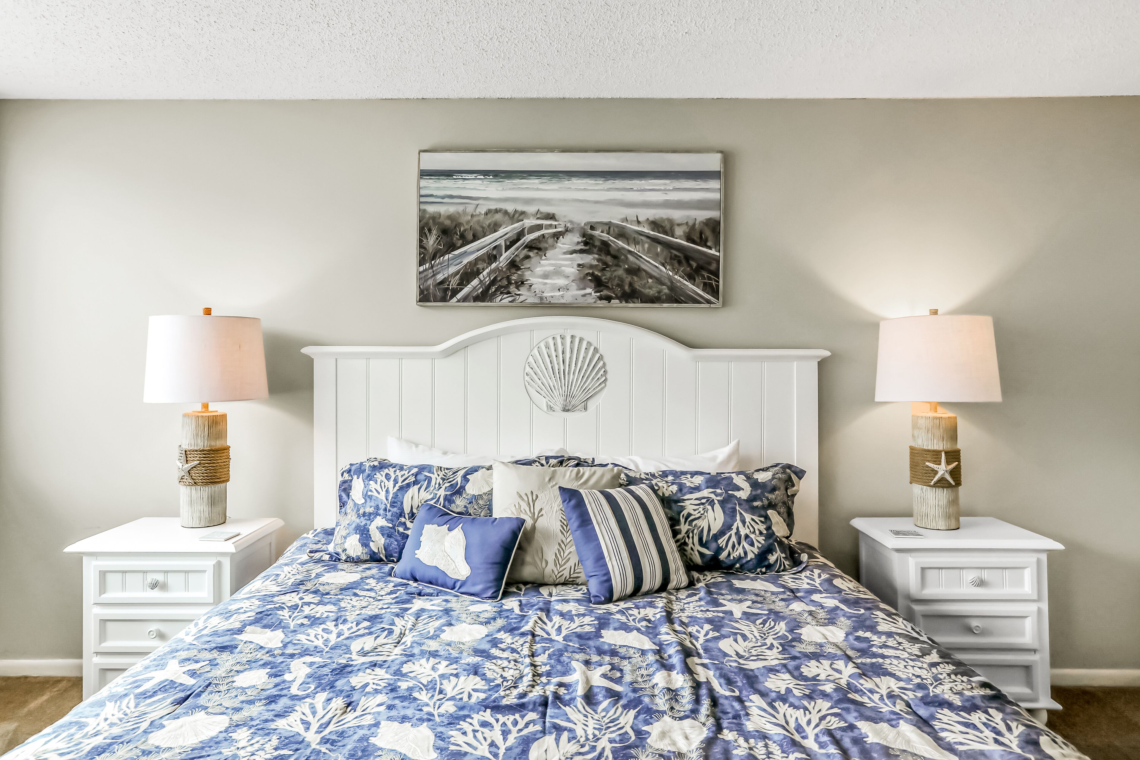 Quarto com cama, duas mesas de cabeceira, um quadro na parede e duas luminárias.