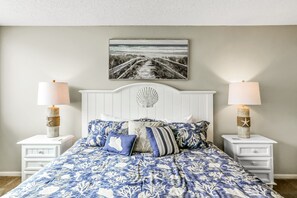 A bedroom with a bed, two nightstands, a wall-mounted picture, and two lamps. - Charming Amelia Island Plantation Condo With Balcony, AC, Washer/dryer & Pool (Fernandina Beach)