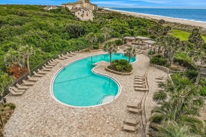 A resort with a large, curved swimming pool surrounded by lounge chairs and palm trees, overlooking a beach. - Charming Amelia Island Plantation Condo With Balcony, AC, Washer/dryer & Pool (Fernandina Beach)