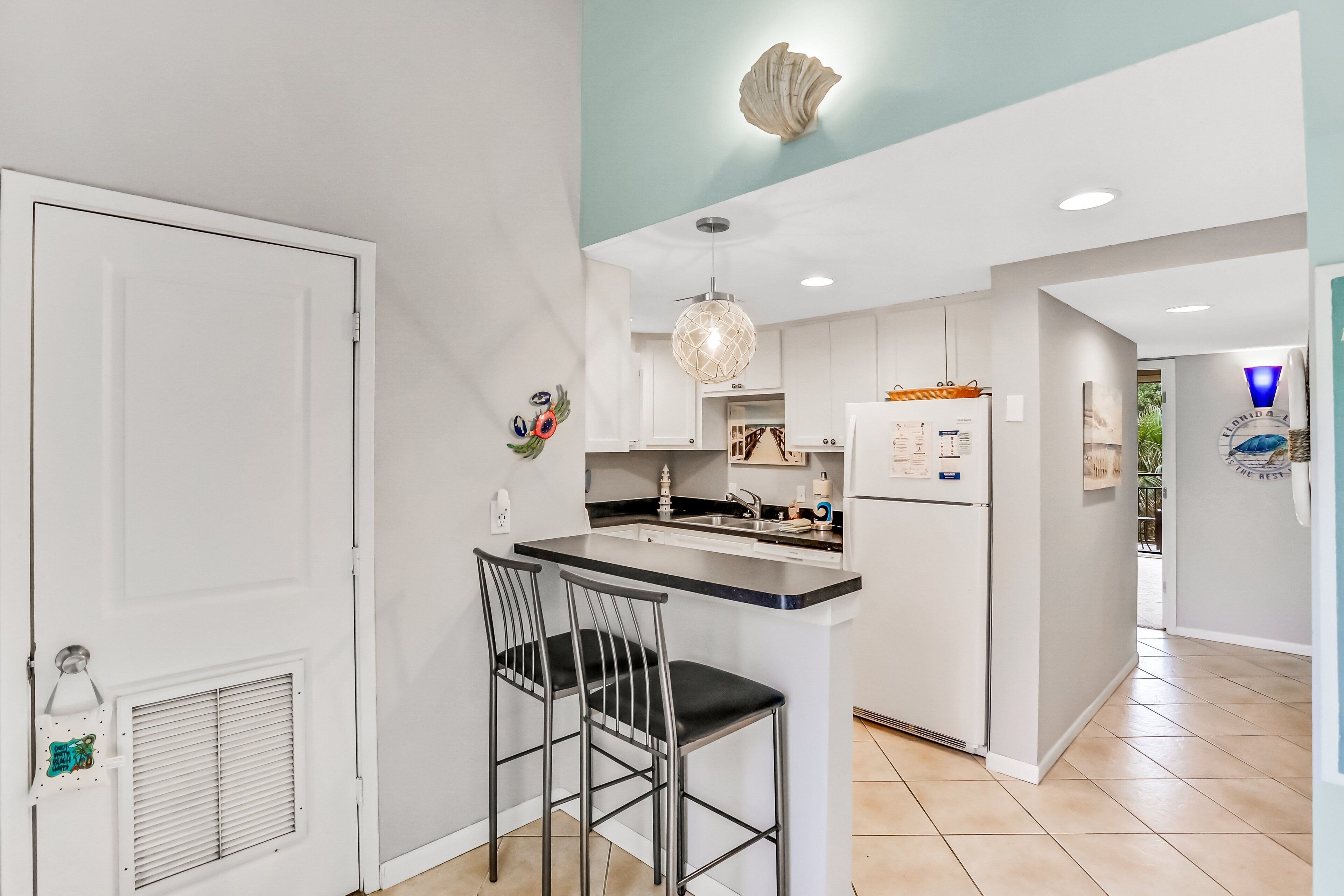 A modern kitchen with white cabinetry, a black countertop, and two bar stools.