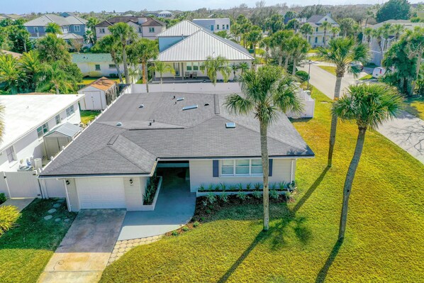 A modern house with a garage, a covered patio, and a well-maintained lawn with palm trees. - Beachside Snowbird Escape With Fenced Yard & Washer/dryer - Walk to Beach Access (Jacksonville Beach)