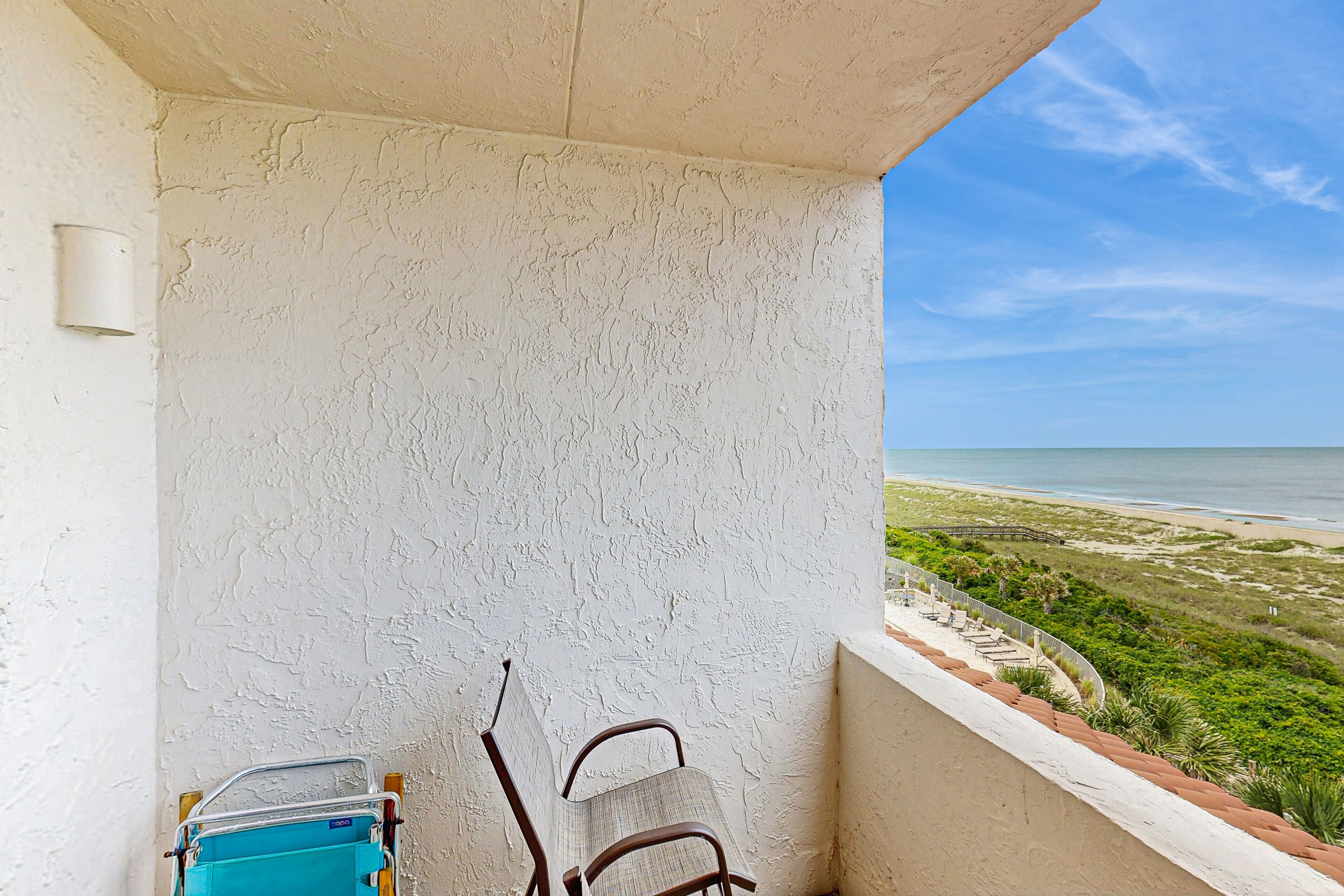 Ein Balkon mit Blick auf den Strand, ein Stuhl und ein Koffer.