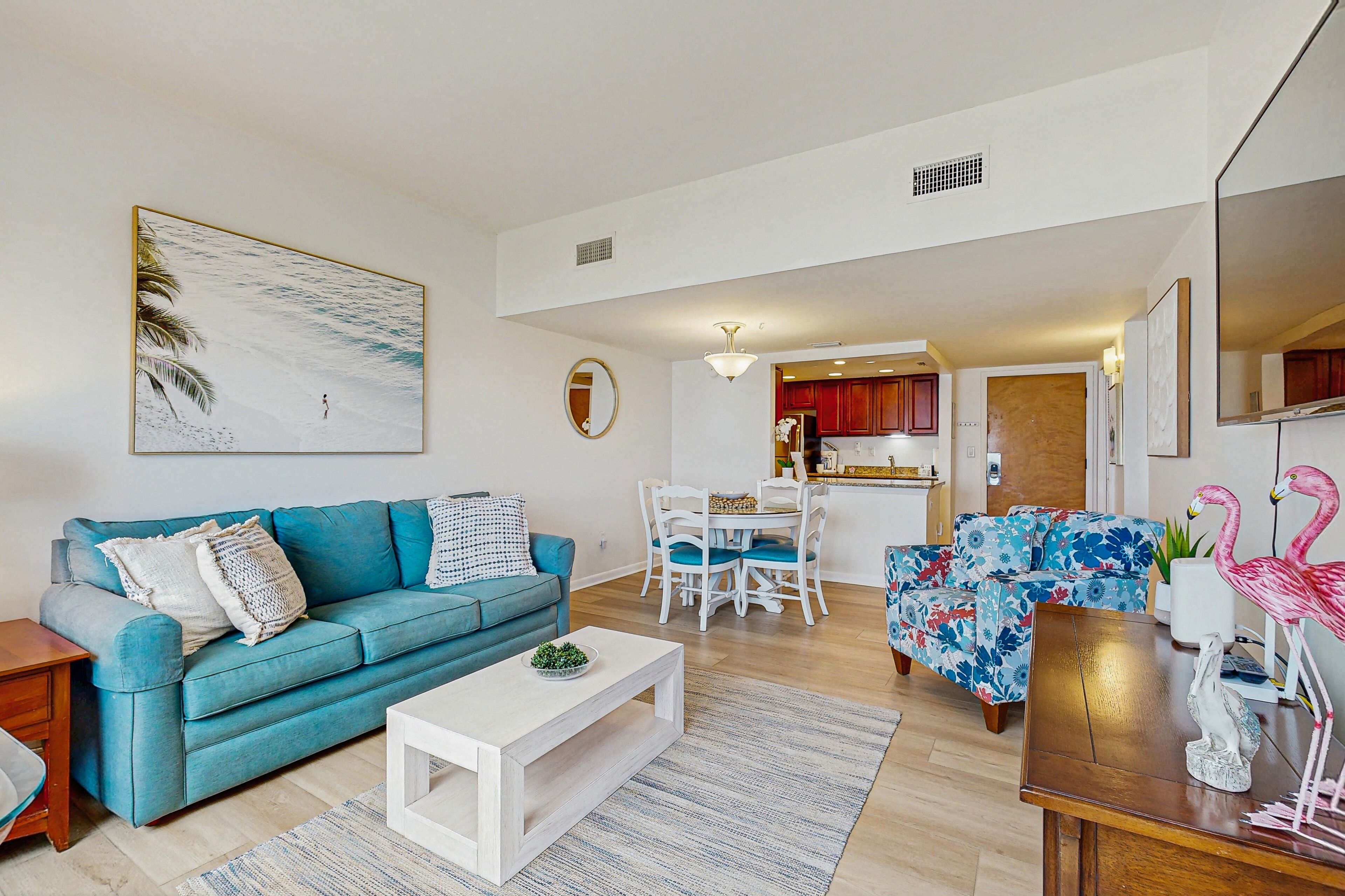 A modern living room with a blue sofa, a white coffee table, and a dining area with a white table and chairs.